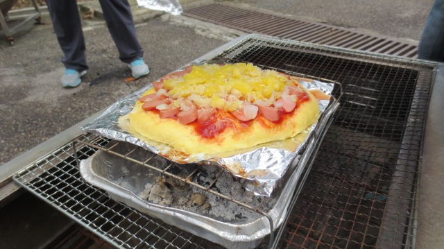 Pizza cooking in a box oven (foil-lined lid (box) removed) over a bed of charcoal at camp - yum
